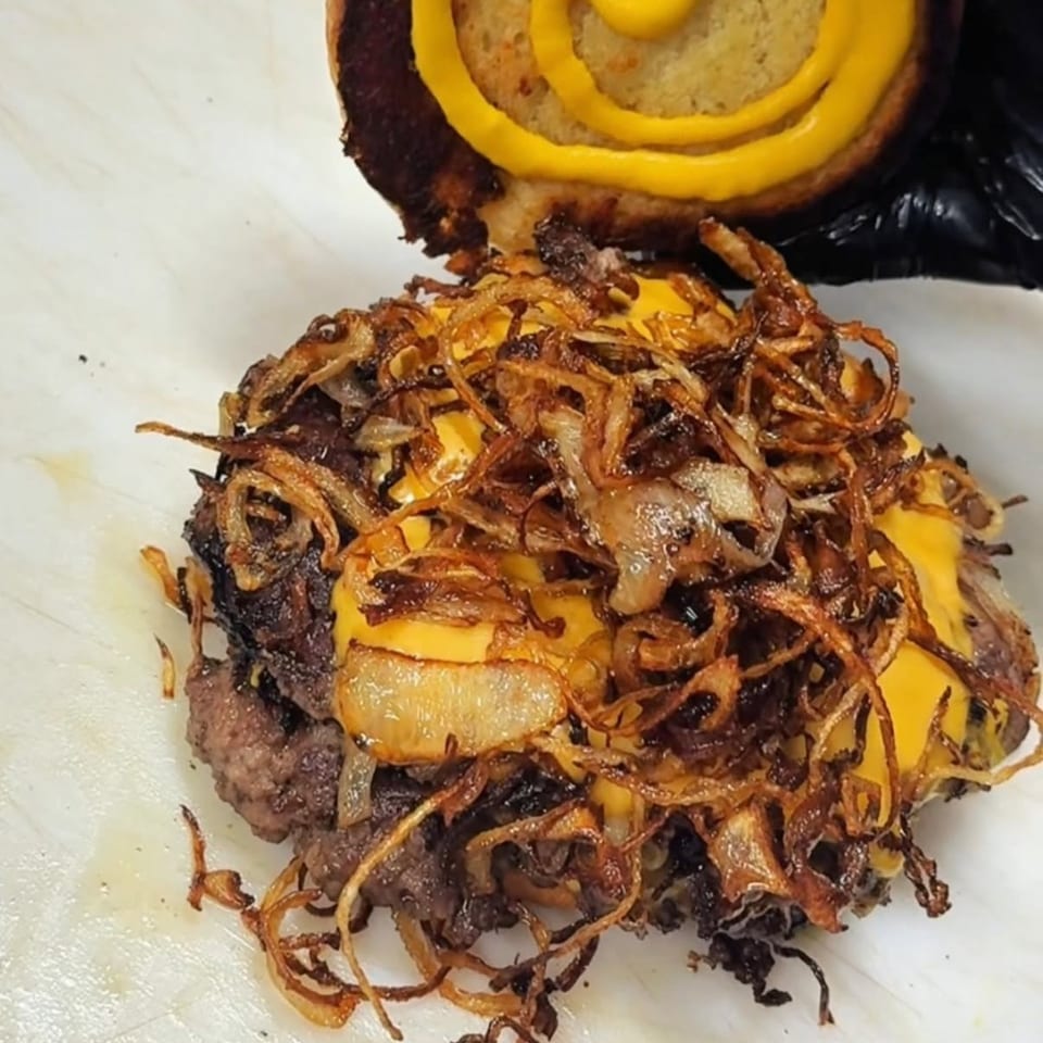 A burger patty with melted cheese and crispy fried onions, with a mustard-swirled bun above.