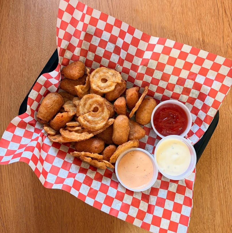 Basket of fried corn dog bites and curly fries with ketchup, ranch, and spicy mayo.